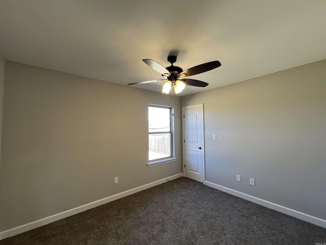 spare room featuring a ceiling fan, dark colored carpet, and baseboards