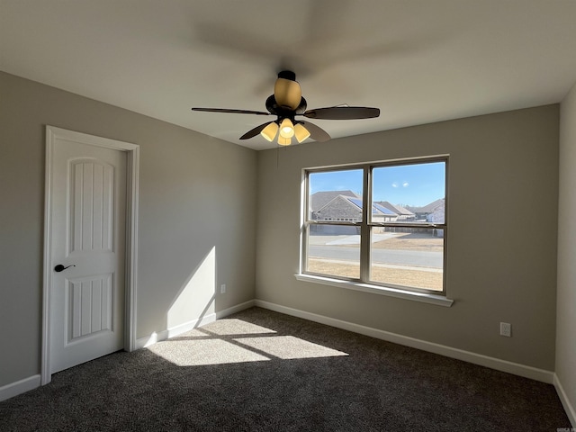 unfurnished room featuring dark carpet, a ceiling fan, and baseboards