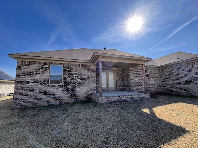 back of property with a patio area, roof with shingles, a yard, and brick siding