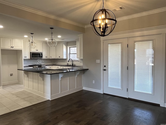 kitchen with a peninsula, white cabinets, stainless steel microwave, dark countertops, and crown molding