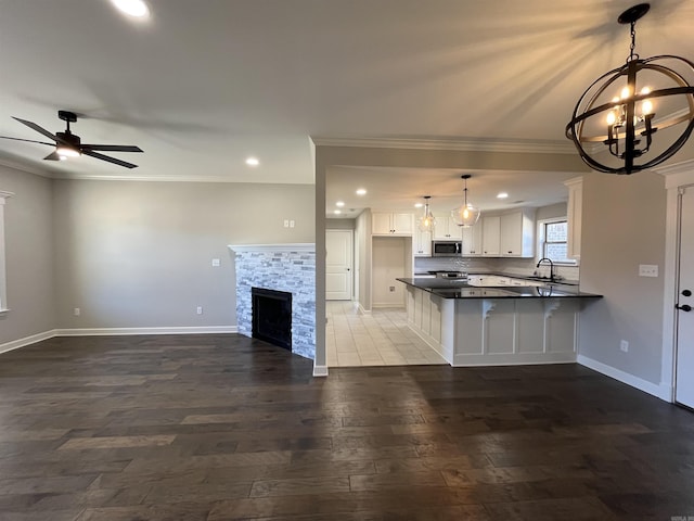 kitchen featuring dark countertops, stainless steel microwave, open floor plan, a sink, and a stone fireplace