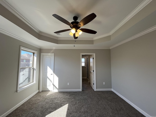 unfurnished bedroom featuring multiple windows, baseboards, a raised ceiling, and dark colored carpet