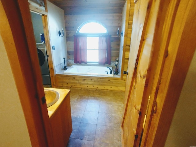 full bathroom featuring washer / dryer, tile patterned floors, a bathtub, vanity, and wood walls