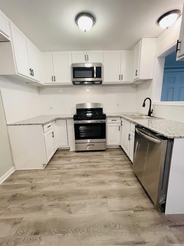 kitchen featuring light stone counters, backsplash, appliances with stainless steel finishes, light wood-style floors, and a sink