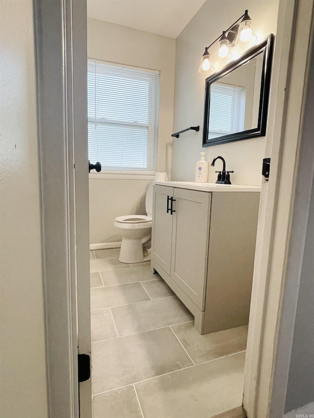 half bath featuring baseboards, vanity, toilet, and tile patterned floors