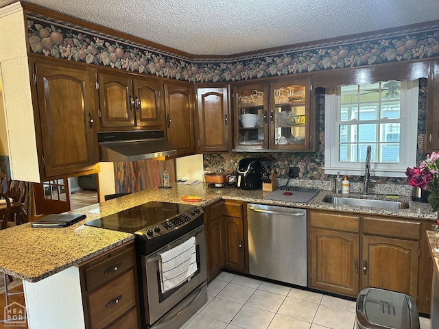 kitchen with glass insert cabinets, appliances with stainless steel finishes, a textured ceiling, under cabinet range hood, and a sink