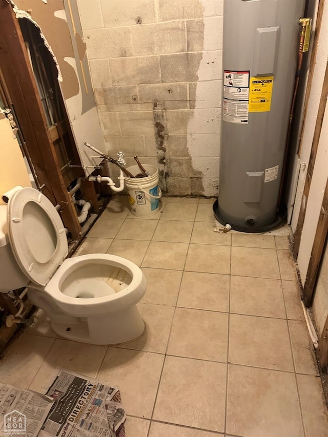 bathroom featuring toilet, tile patterned flooring, water heater, and concrete block wall