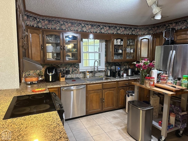 kitchen featuring appliances with stainless steel finishes, glass insert cabinets, light tile patterned flooring, a sink, and a textured ceiling