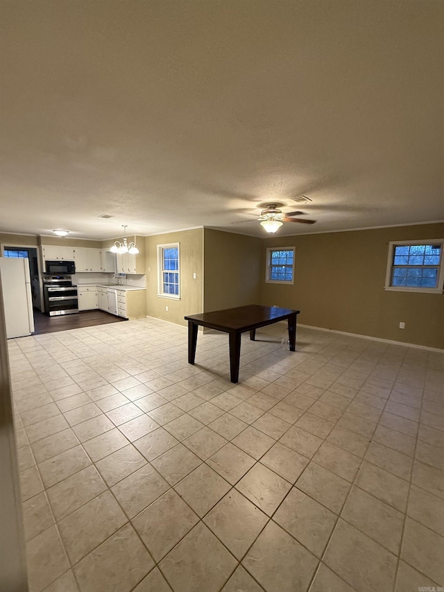 game room featuring ceiling fan with notable chandelier, plenty of natural light, a textured ceiling, light tile patterned floors, and baseboards