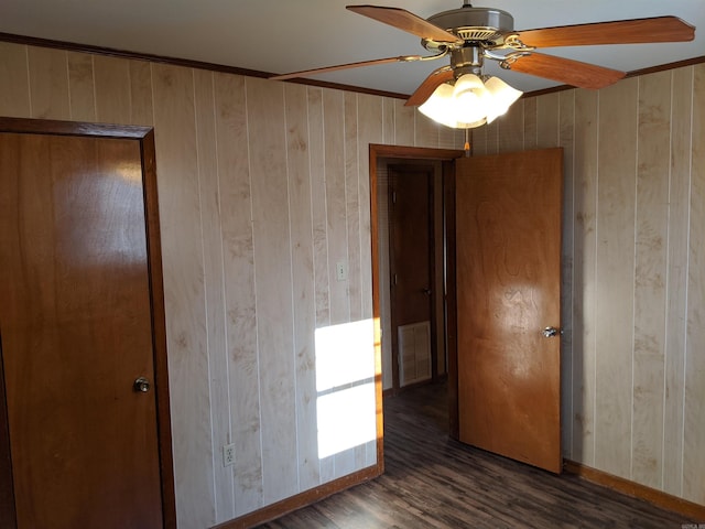 unfurnished bedroom with ceiling fan, wooden walls, visible vents, and wood finished floors