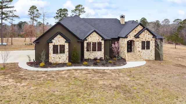 french country home featuring stone siding, a chimney, and roof with shingles