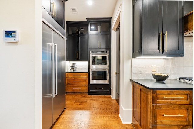 kitchen with visible vents, light wood-style floors, appliances with stainless steel finishes, decorative backsplash, and dark countertops