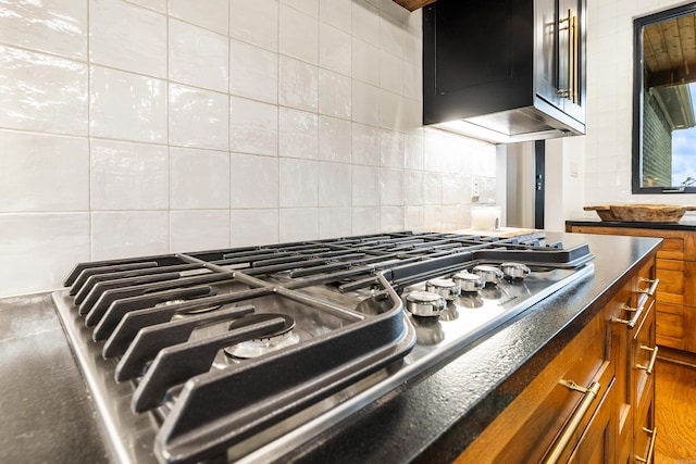 interior details featuring brown cabinetry, dark countertops, decorative backsplash, and stainless steel gas stovetop