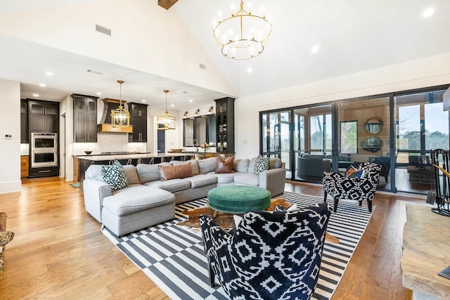 living room featuring high vaulted ceiling, light wood-style floors, visible vents, and a notable chandelier