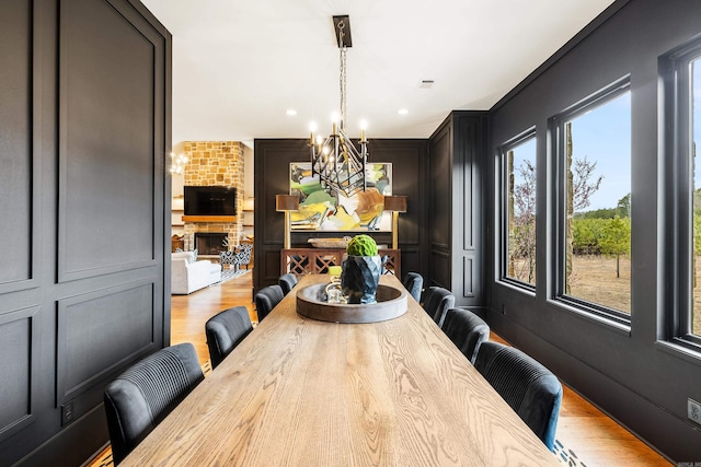 dining space featuring visible vents, wood finished floors, a fireplace, a decorative wall, and a notable chandelier