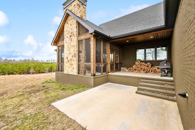 exterior space featuring a patio, a sunroom, stone siding, a chimney, and roof with shingles