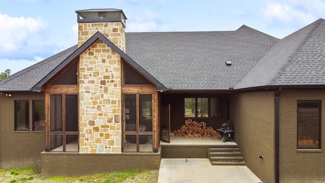 back of house featuring a shingled roof, a chimney, and brick siding