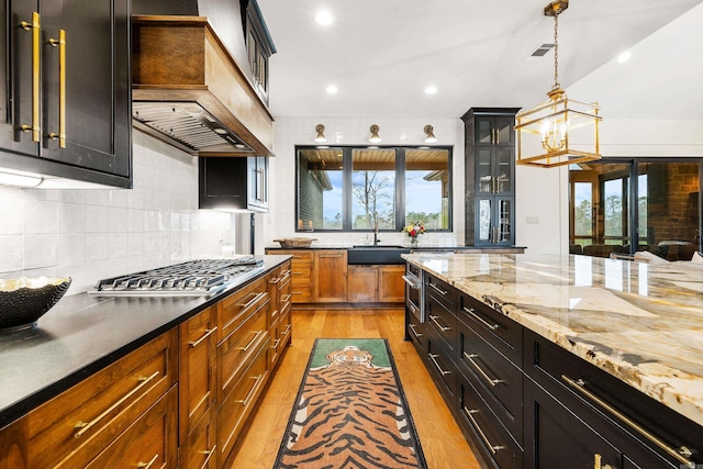 kitchen featuring custom range hood, stainless steel gas stovetop, decorative backsplash, light wood-style floors, and a sink