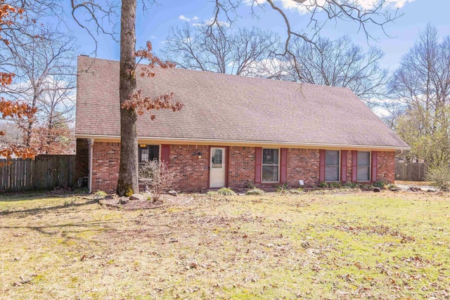 view of front of house with a shingled roof, fence, a front lawn, and brick siding