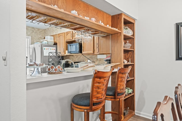 kitchen with a breakfast bar area, light countertops, freestanding refrigerator, black microwave, and baseboards