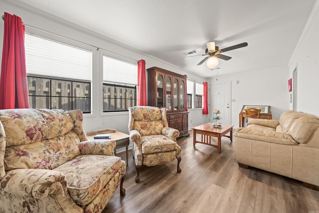 living area featuring a ceiling fan, visible vents, ornamental molding, and wood finished floors