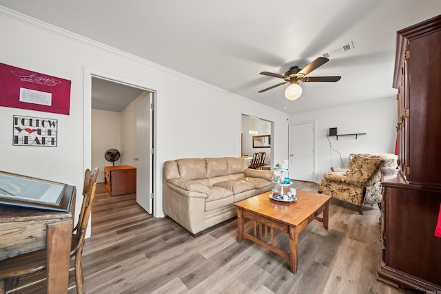 living area featuring light wood-style floors, visible vents, crown molding, and ceiling fan