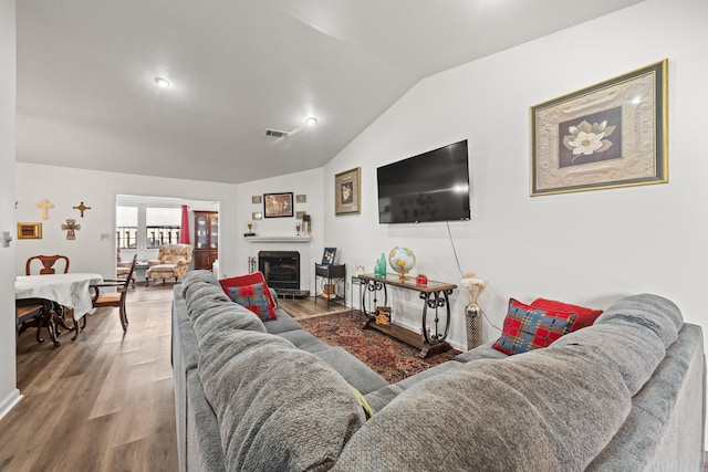 living area with a fireplace with raised hearth, vaulted ceiling, visible vents, and wood finished floors