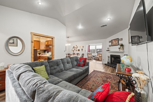 living room with a fireplace with raised hearth, visible vents, vaulted ceiling, and wood finished floors