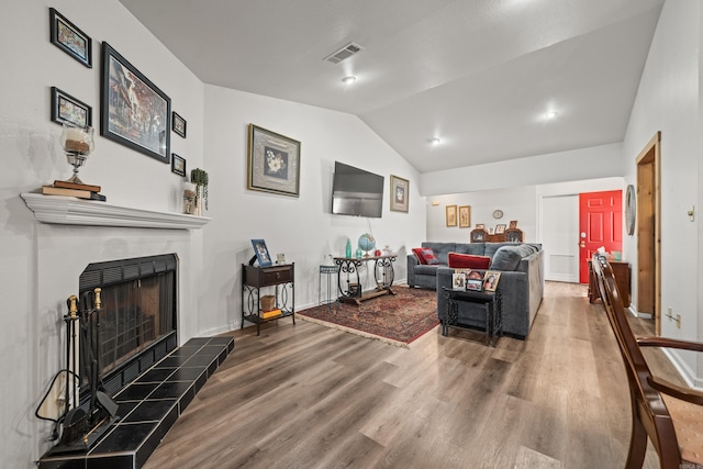 living room with baseboards, visible vents, a tiled fireplace, lofted ceiling, and wood finished floors