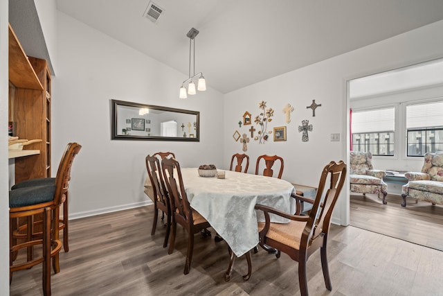 dining room with lofted ceiling, wood finished floors, visible vents, and baseboards