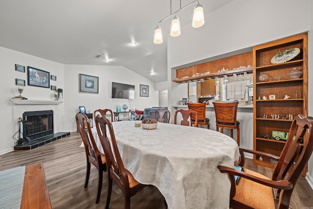 dining space featuring vaulted ceiling, a tiled fireplace, wood finished floors, and visible vents