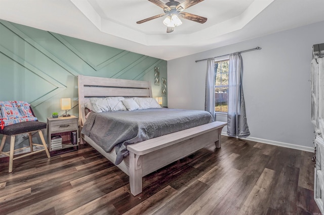 bedroom with a tray ceiling, wood finished floors, a ceiling fan, and baseboards