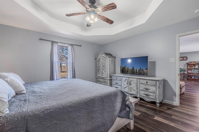 bedroom with baseboards, a tray ceiling, ceiling fan, and dark wood-type flooring