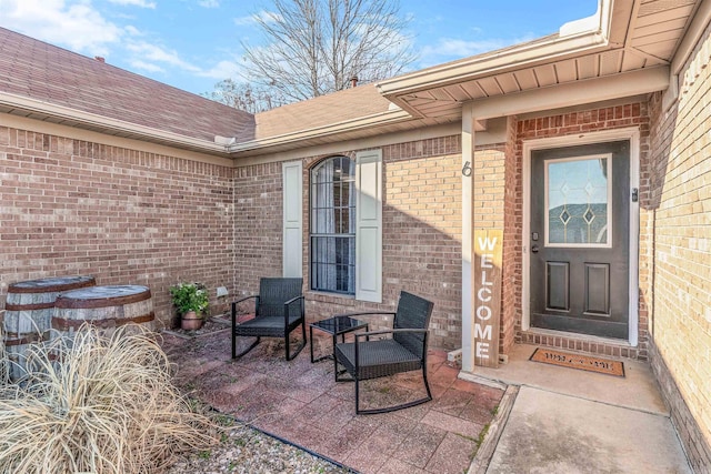 view of exterior entry with a patio area, roof with shingles, and brick siding