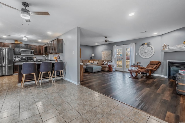 living room with light tile patterned floors, french doors, a glass covered fireplace, and a ceiling fan