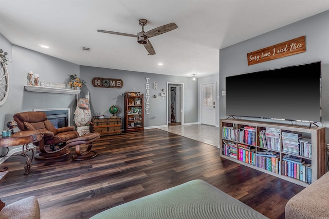 living area with ceiling fan, wood finished floors, visible vents, baseboards, and a glass covered fireplace