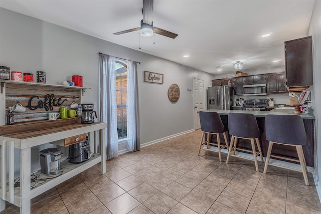 kitchen featuring a breakfast bar area, dark brown cabinetry, stainless steel appliances, a peninsula, and a ceiling fan