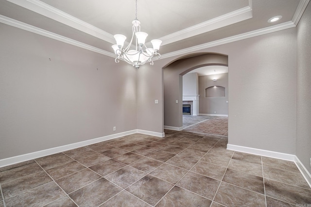 spare room featuring baseboards, a tray ceiling, a glass covered fireplace, and ornamental molding