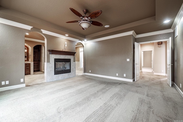 unfurnished living room featuring carpet floors, arched walkways, a raised ceiling, a textured wall, and a tile fireplace