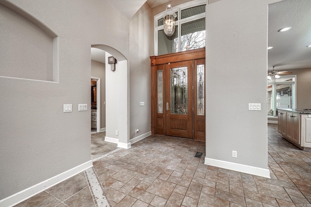 foyer with arched walkways, stone finish flooring, baseboards, and ceiling fan with notable chandelier