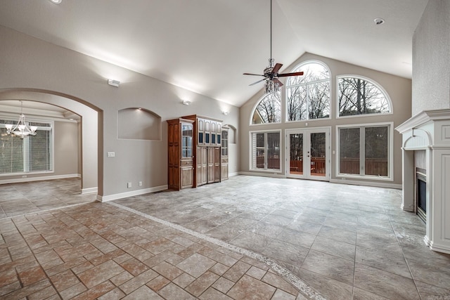 unfurnished living room with arched walkways, high vaulted ceiling, ceiling fan with notable chandelier, baseboards, and a glass covered fireplace