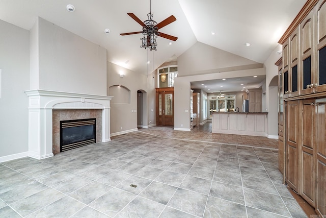 unfurnished living room with a tiled fireplace, a ceiling fan, light tile patterned flooring, high vaulted ceiling, and baseboards