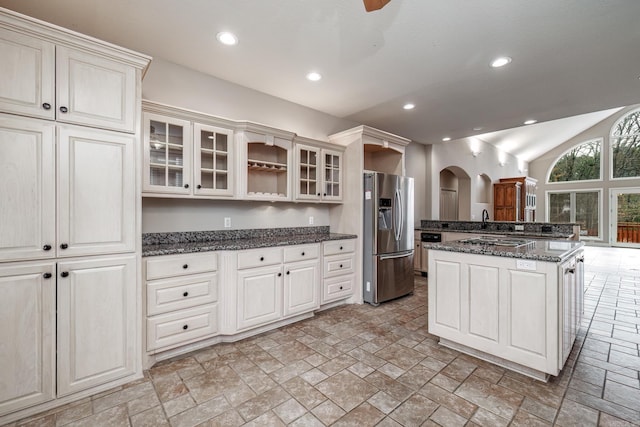 kitchen with arched walkways, recessed lighting, vaulted ceiling, stainless steel fridge, and glass insert cabinets