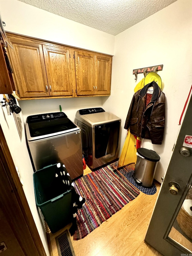 washroom with cabinet space, visible vents, washer and clothes dryer, wood finished floors, and a textured ceiling