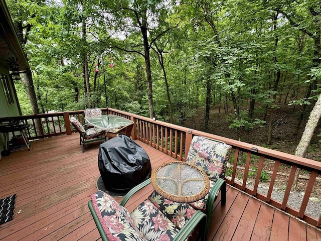 wooden terrace with outdoor dining space, grilling area, and a view of trees