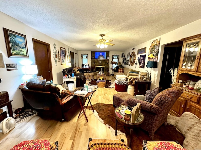 living room with a glass covered fireplace, ceiling fan, light wood-style flooring, and a textured ceiling