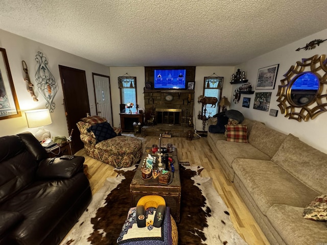 living area featuring a stone fireplace, a textured ceiling, and wood finished floors