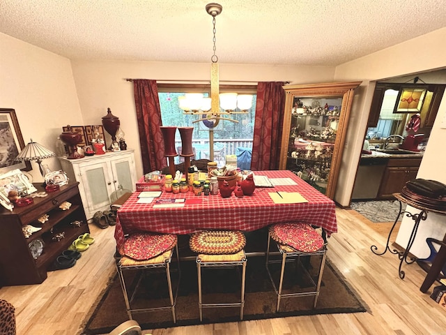 dining space with light wood-style floors, a notable chandelier, and a textured ceiling