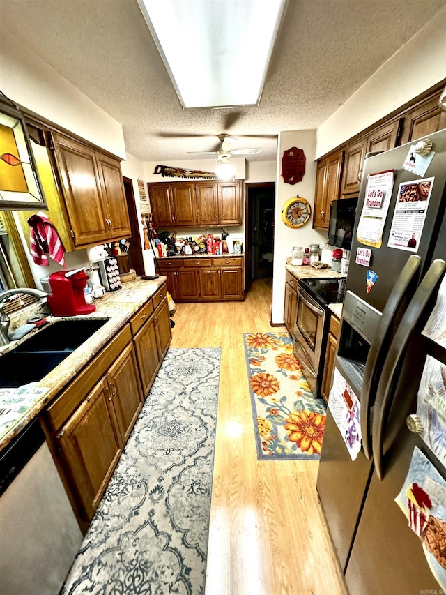 kitchen featuring a textured ceiling, stainless steel appliances, light wood finished floors, and a sink