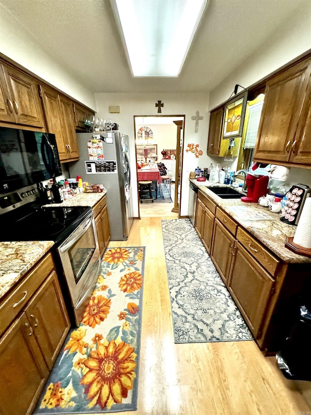 kitchen featuring appliances with stainless steel finishes, brown cabinetry, a sink, and light wood finished floors